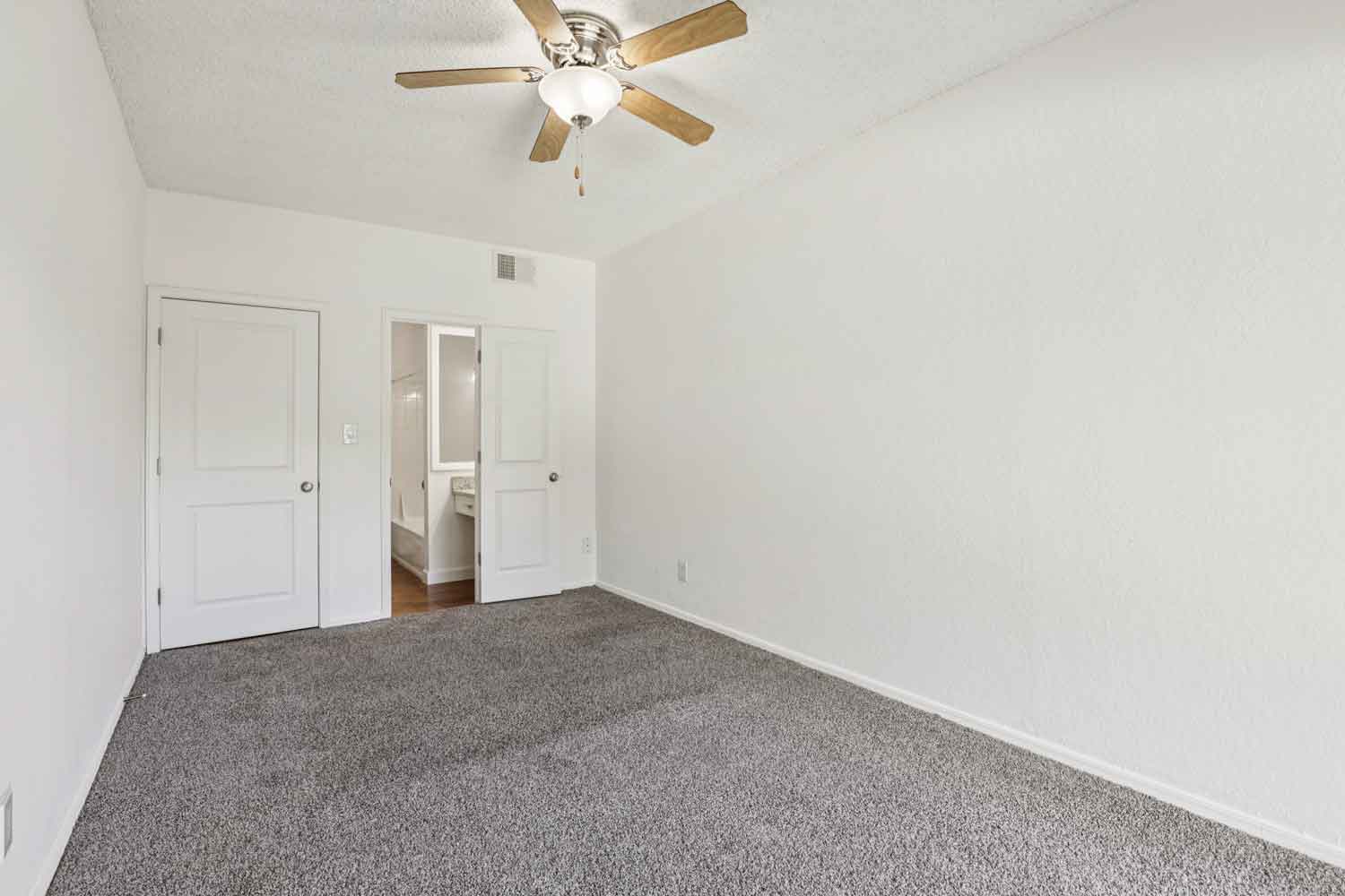 Carpeted bedroom with ceiling fan, white walls, and double doors leading to bathroom and closet