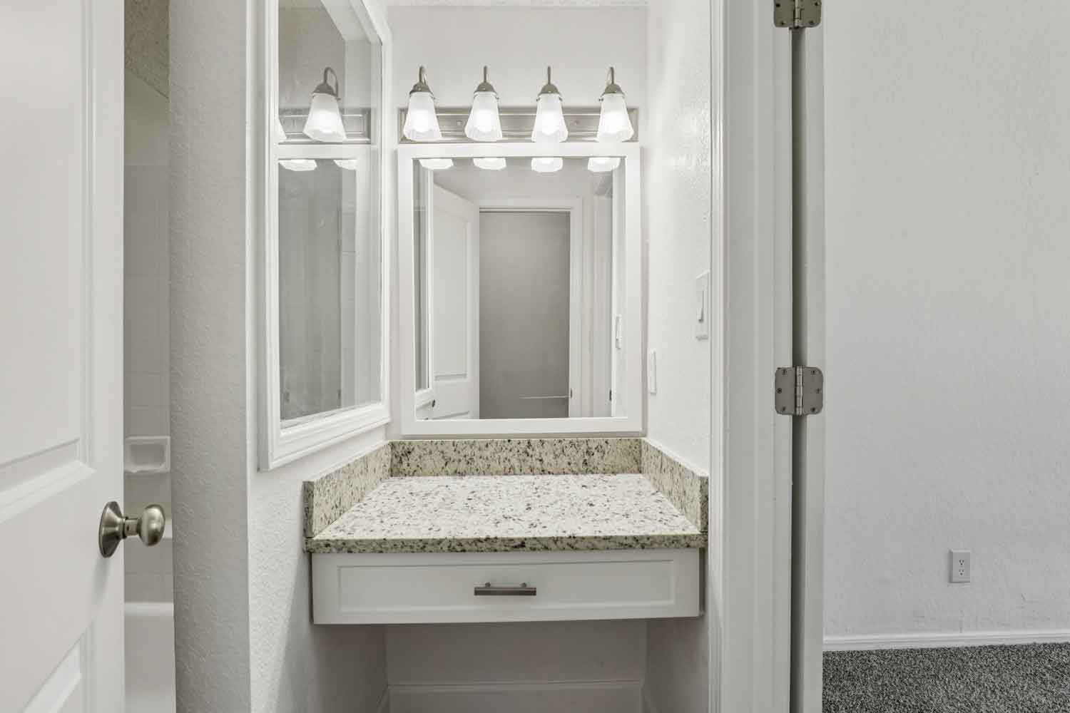 Bathroom vanity with granite countertop, white cabinetry, framed mirrors, and five light fixture above sink