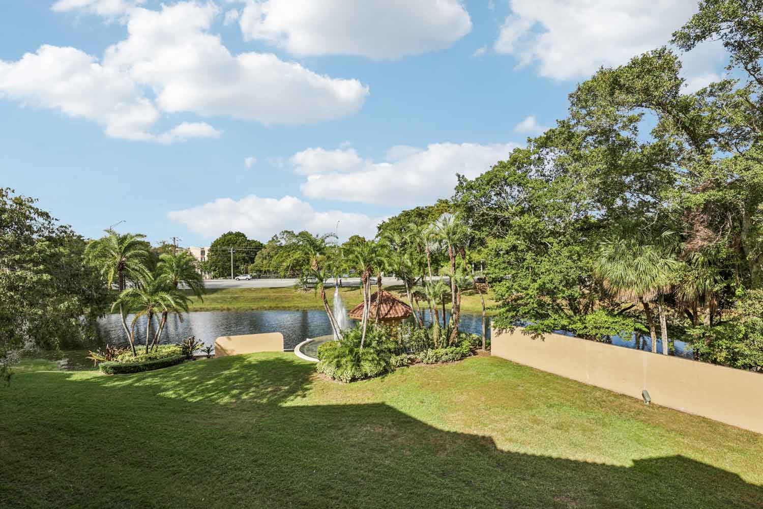 Lakeside lawn with palm trees, gazebo, and water feature beyond landscaped wall