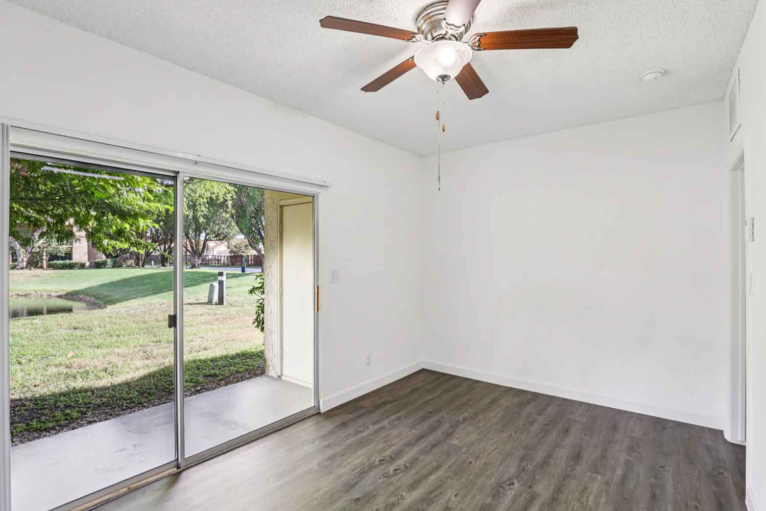 Living area with wood style flooring, ceiling fan, and sliding glass doors opening to patio with pond view