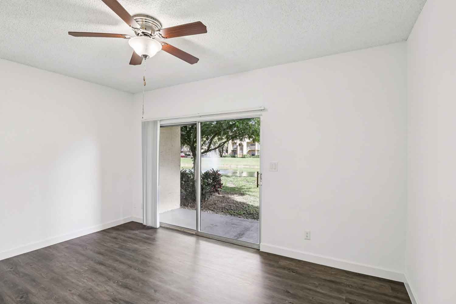 Open living space with wood style flooring, ceiling fan, and sliding glass doors leading to a covered patio