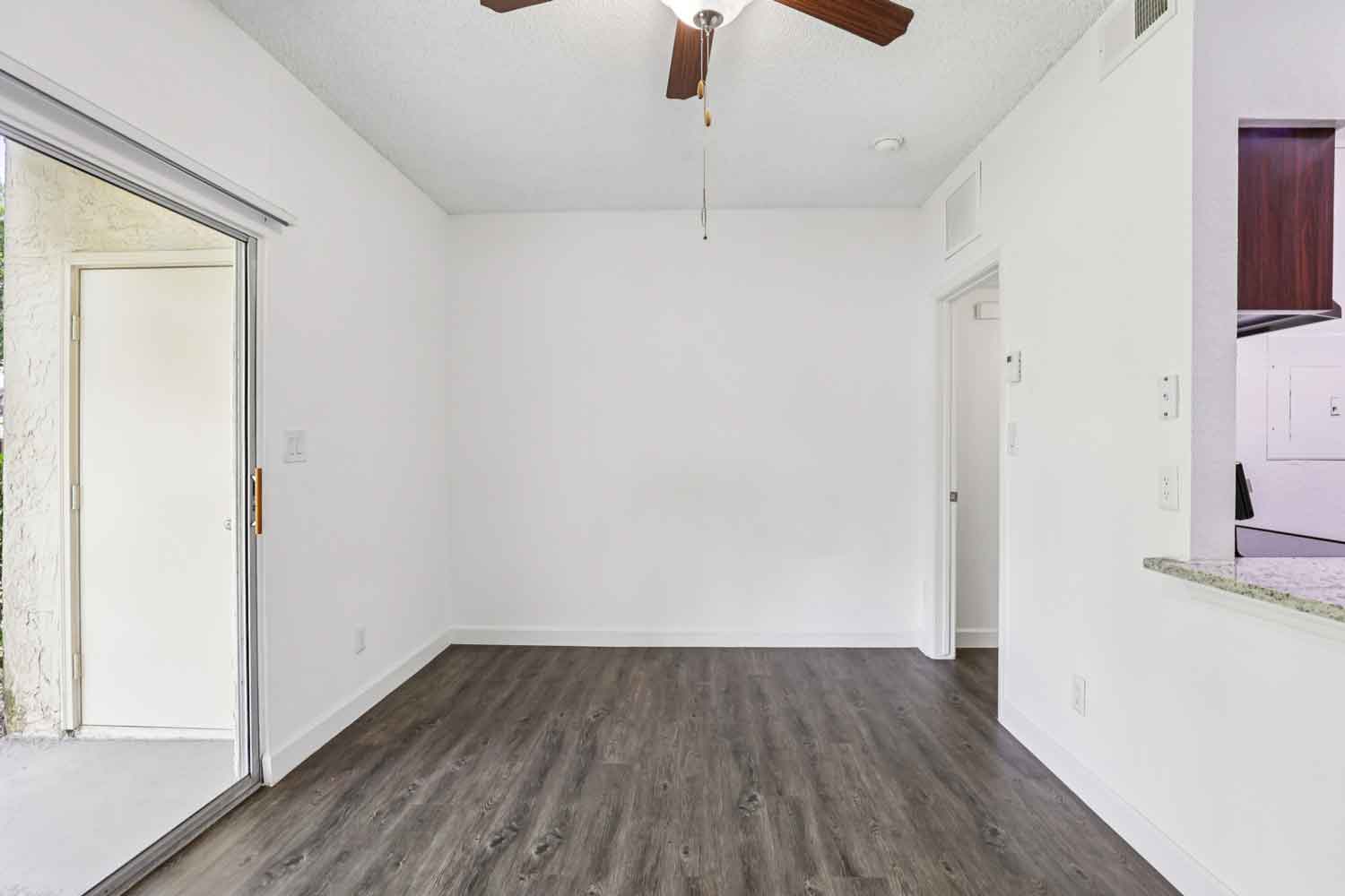 Bright living room with wood style flooring, white walls, ceiling fan, and sliding glass door opening to a private patio