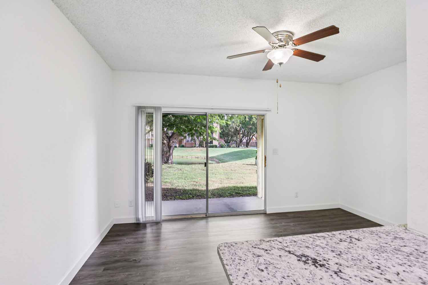 Spacious living room with wood style flooring, ceiling fan, sliding glass doors, and natural light from patio view