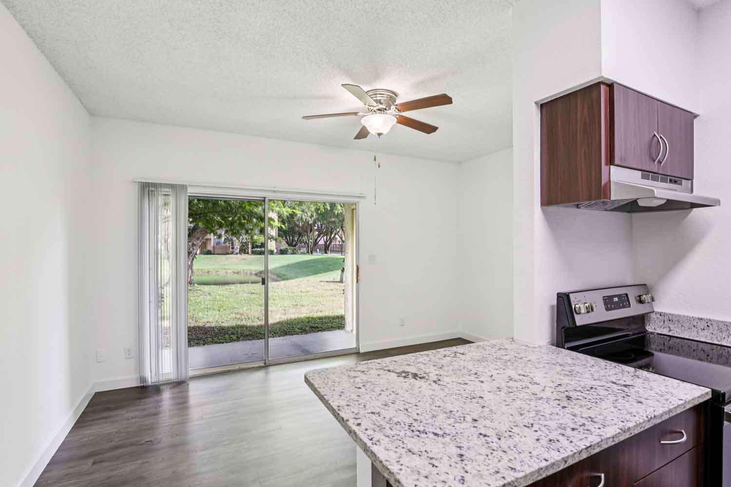 Living area with sliding glass doors, ceiling fan, granite countertop island, and view into kitchen with range
