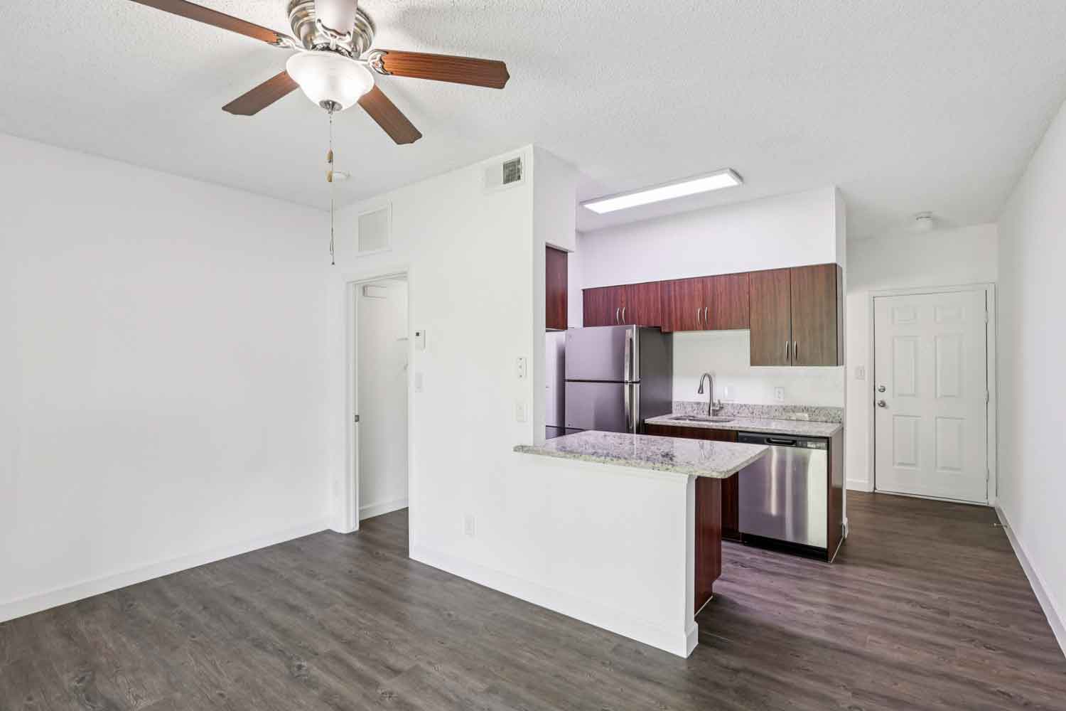 Open living area with wood style flooring, ceiling fan, granite breakfast bar, and kitchen with stainless steel appliances