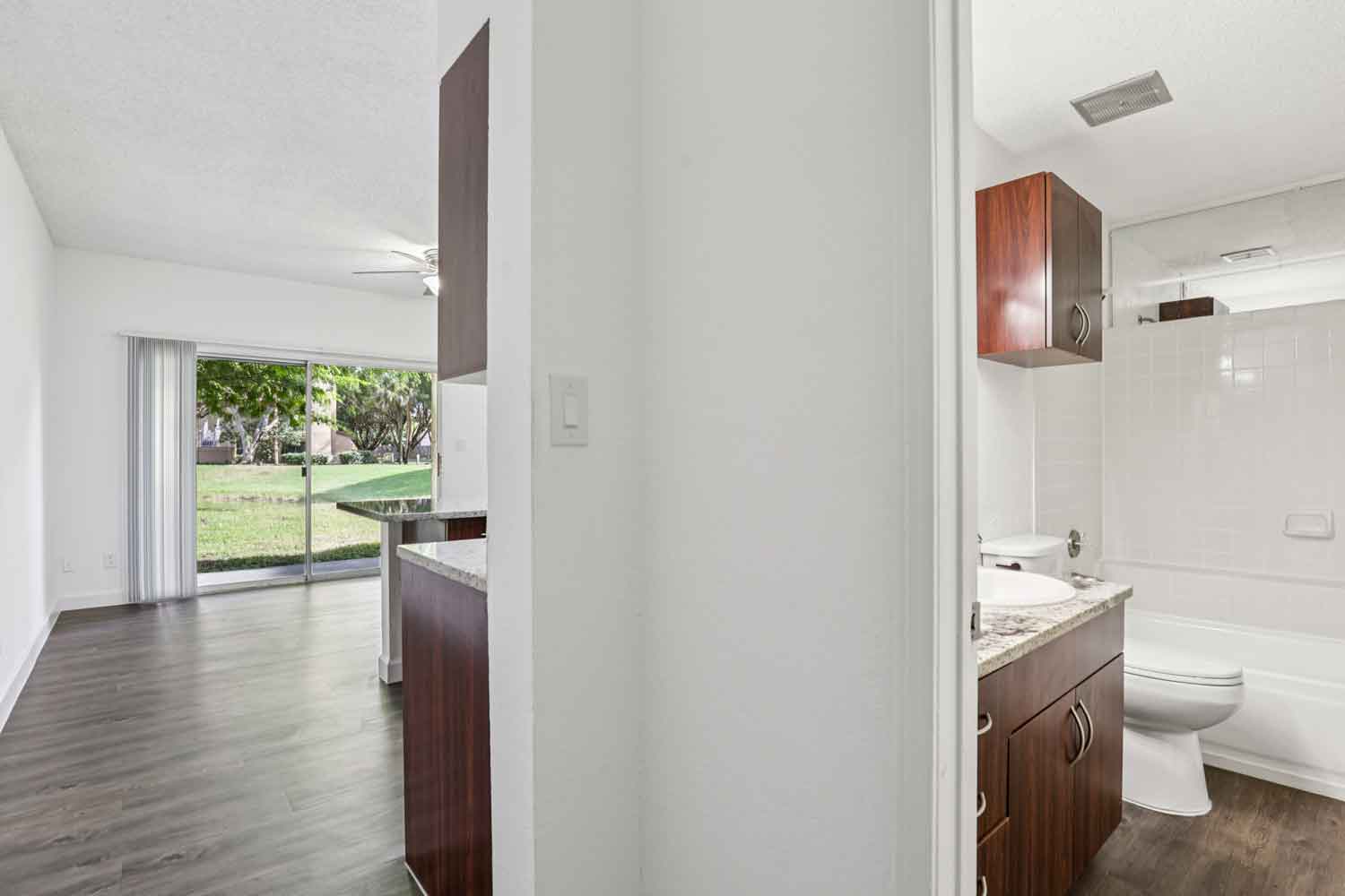 View from hallway into kitchen and bathroom with granite vanity, tub shower combo, and sliding glass doors in living area