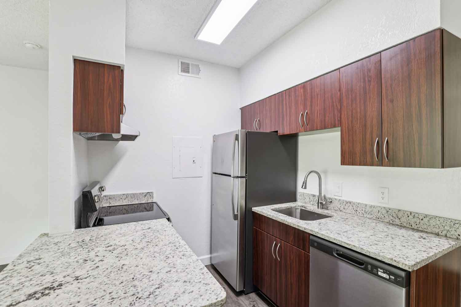 Compact kitchen with granite counters, stainless steel appliances, wood cabinets, and skylight above for natural light