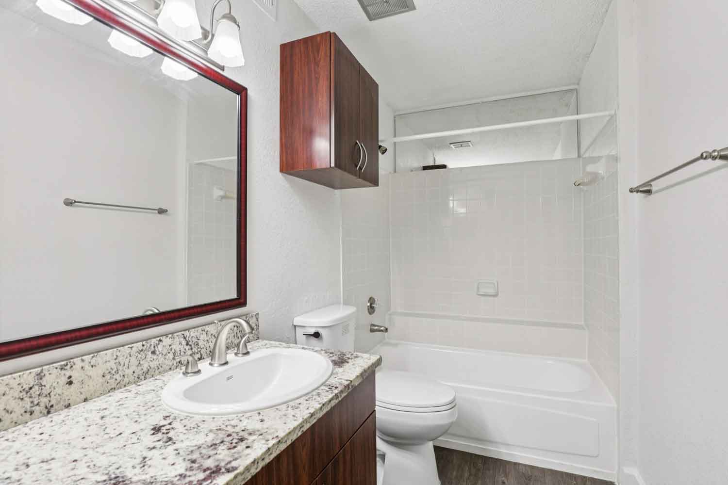 Full bathroom with tub and shower combo, granite countertop, wood vanity cabinet, and overhead storage unit