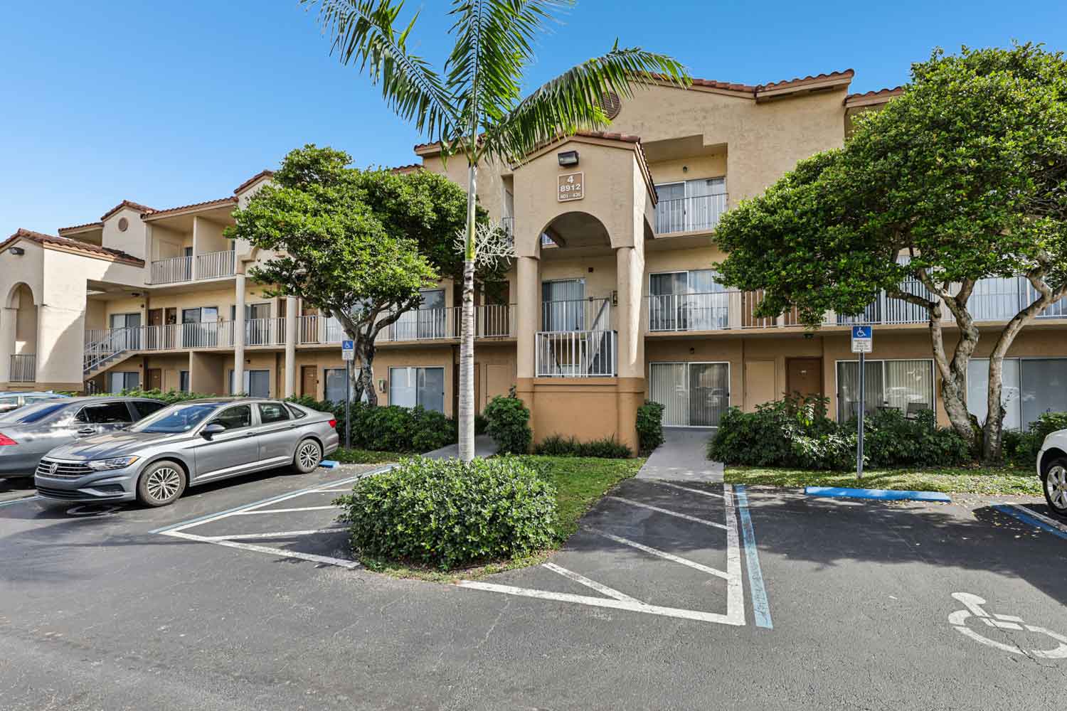 Three story apartment building with arched entry, balconies, and reserved parking spaces