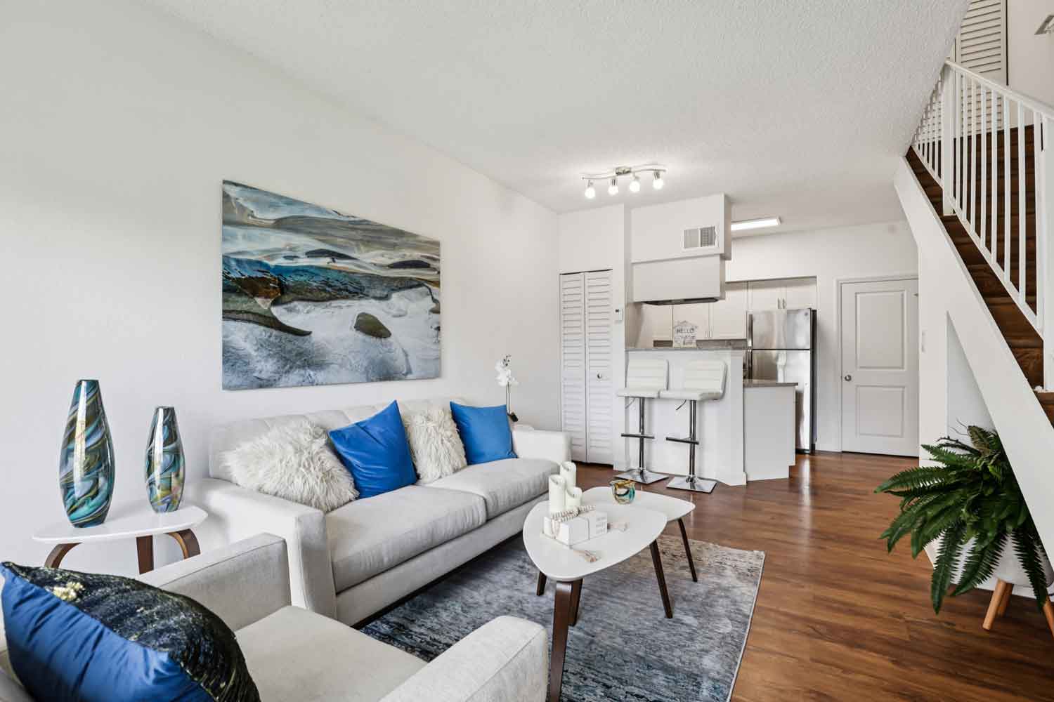 Living room with sofa, armchair, coffee table, staircase, breakfast bar with stools, and stainless steel appliances