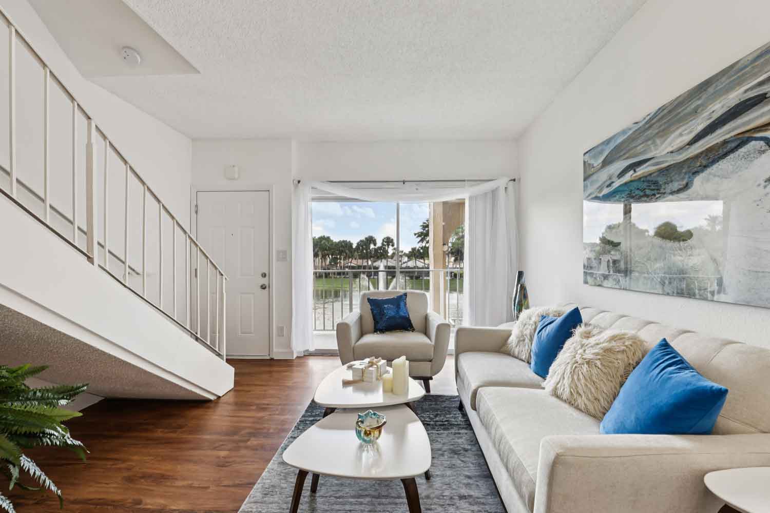 Open living area with wood style flooring, staircase railing, sofa, accent chair, and balcony view of water