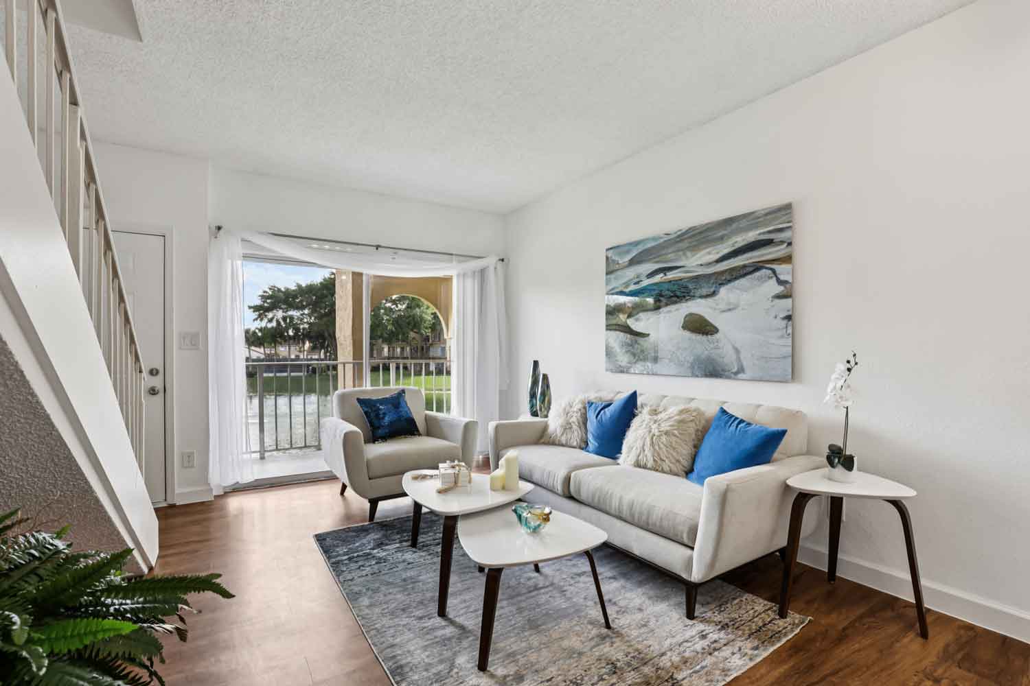 Bright living room with sofa, accent chair, coffee table, staircase, and sliding glass doors overlooking pond
