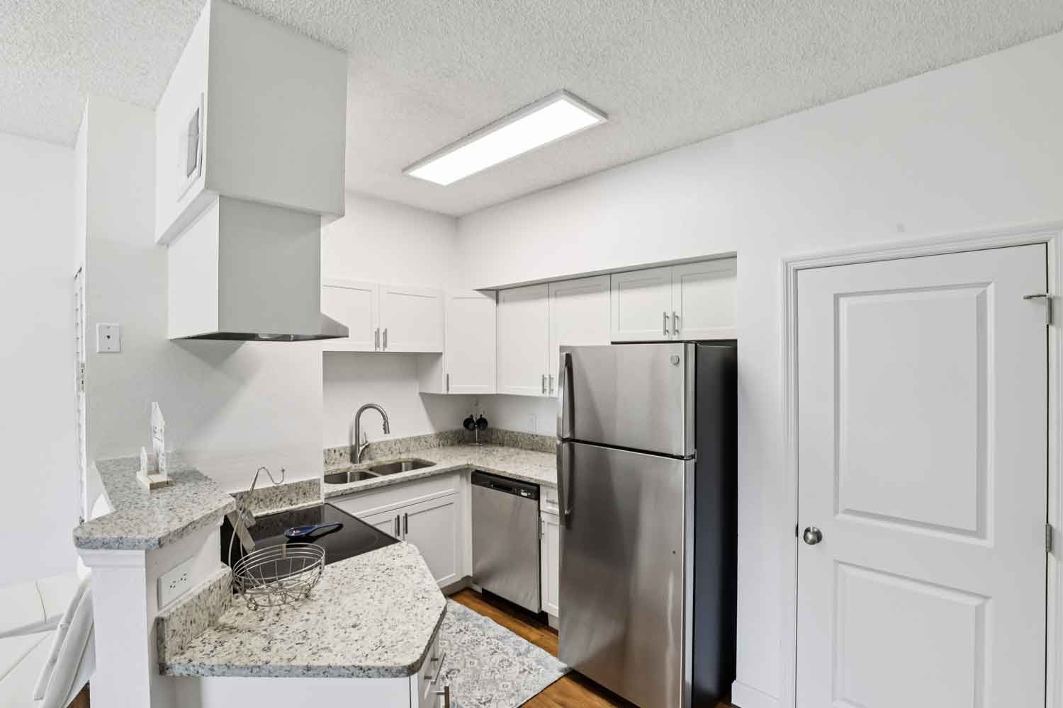 Bright kitchen with granite countertops, stainless steel appliances, white cabinets, and adjacent utility door