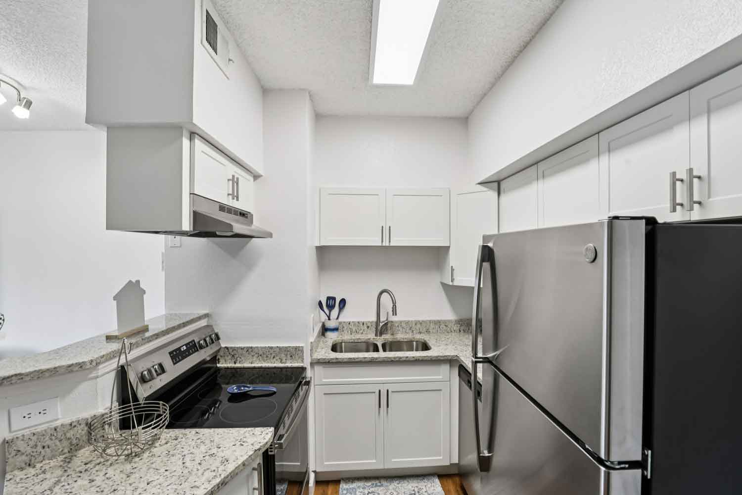 Compact kitchen with stainless steel range, granite breakfast bar, white cabinetry, and overhead lighting
