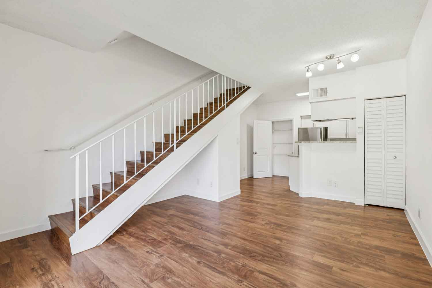 Open concept living and dining area with staircase, wood style flooring, and kitchen with breakfast bar and track lighting