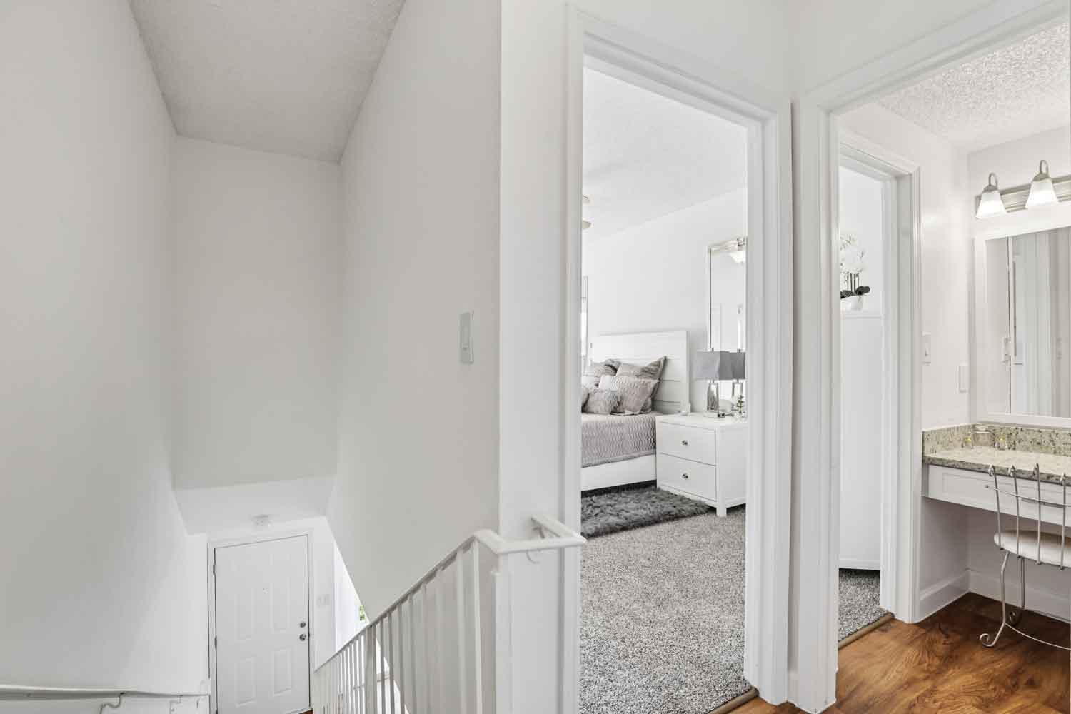 Upstairs hallway with white railing, carpeted bedroom entry, granite vanity nook, and wood style flooring near staircase