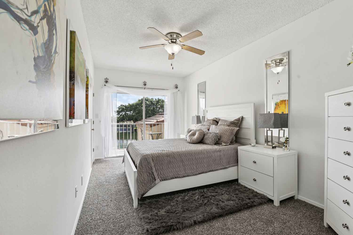 Bright bedroom with sliding glass doors to balcony, ceiling fan, white furniture, and neutral carpet flooring