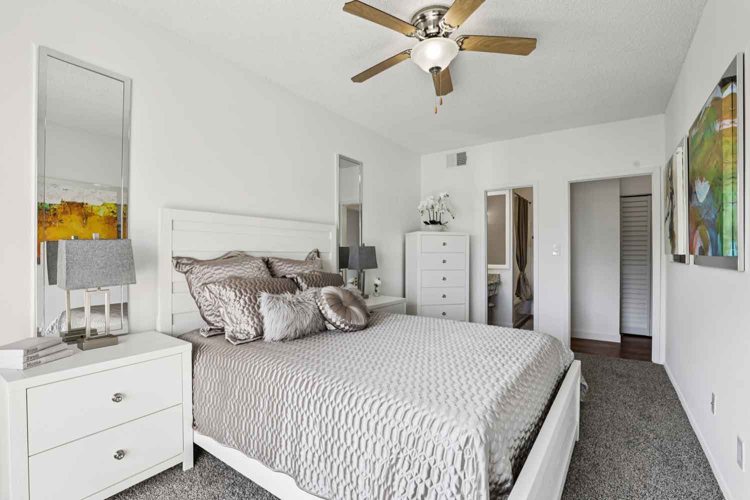 Primary bedroom with white bed frame, textured bedding, ceiling fan, nightstand, and tall dresser with mirror
