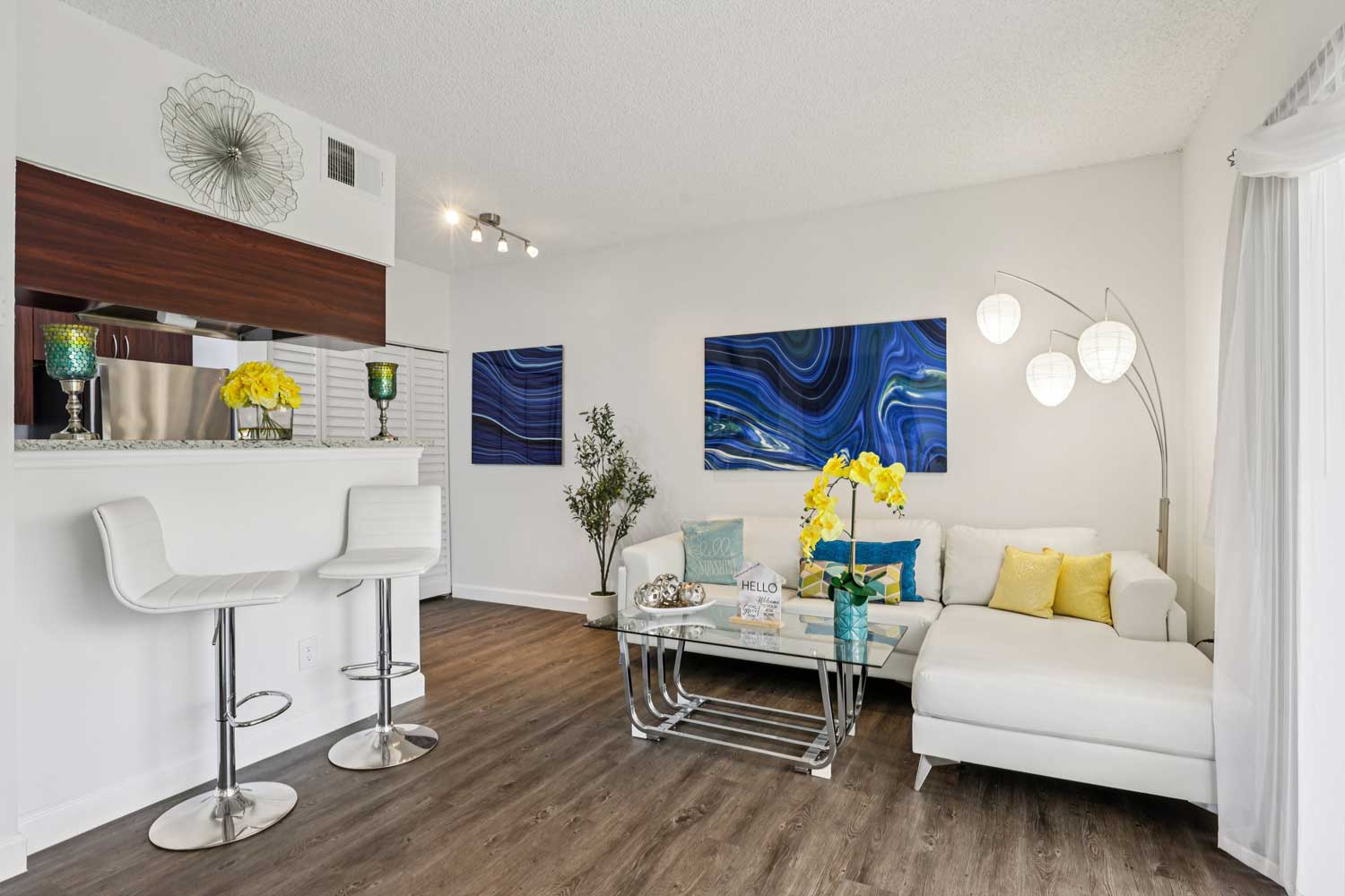 Living area with white bar stools, pass through kitchen, wood style flooring, and bright overhead lighting