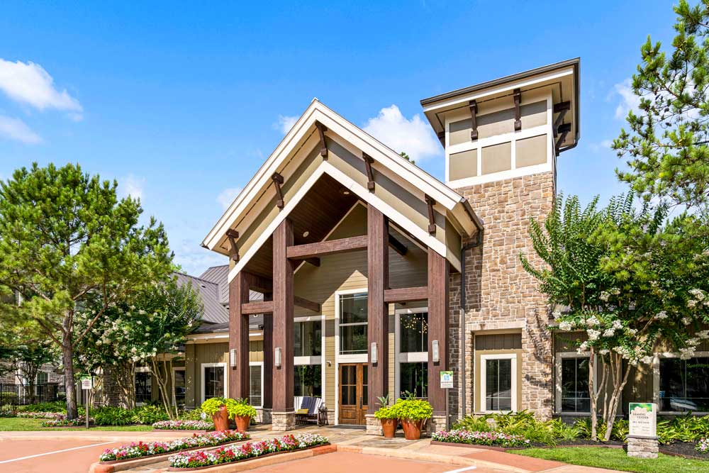 Clubhouse entrance with stone and wood design, flower planters, and clear blue skies overhead