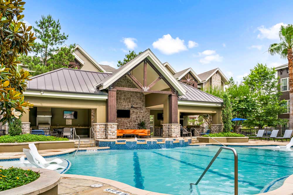 View of the clubhouse pavilion from the pool, with built-in water loungers and lush landscaping all around