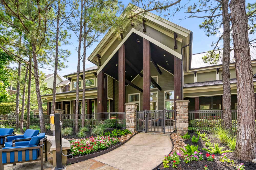 Walkway leading to the clubhouse entrance, featuring tall pillars, trees, and landscaped garden beds