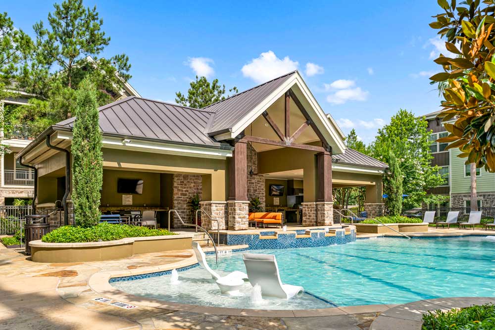 View of a spacious pool with water loungers and a shaded clubhouse pavilion offering orange seating and TVs