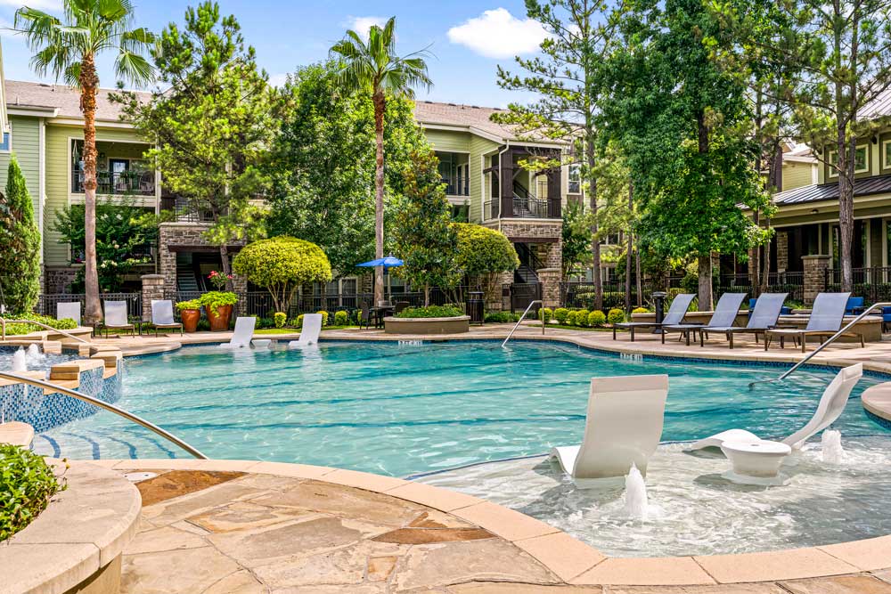 Refreshing swimming pool with water loungers, trees, and neatly landscaped apartment buildings in the background