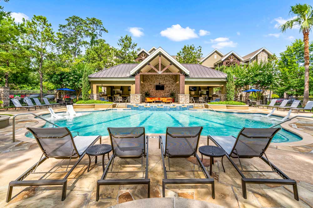 Poolside loungers and tables arranged neatly in front of a resort-style pool and stone-accented clubhouse