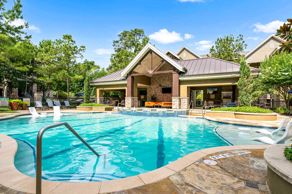 Resort-style swimming pool with submerged loungers, water features, and a clubhouse with shaded seating area