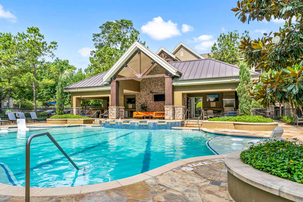 Covered outdoor pavilion with orange seating and TVs, facing the pool with steps and floral landscaping