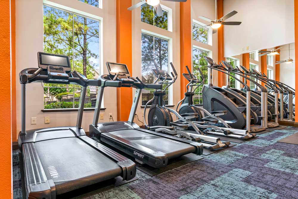 Bright gym with Spirit treadmills and elliptical machines lined up against large windows and orange accent walls
