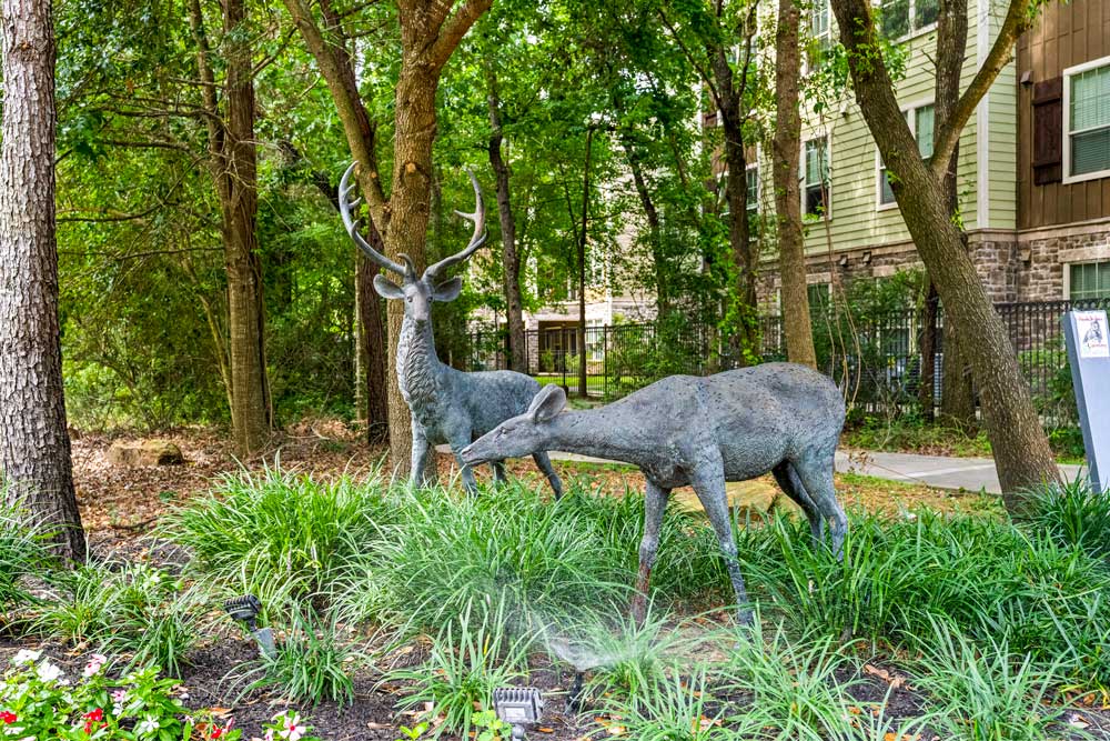 Metal deer sculptures surrounded by lush greenery near apartment buildings in a wooded community setting