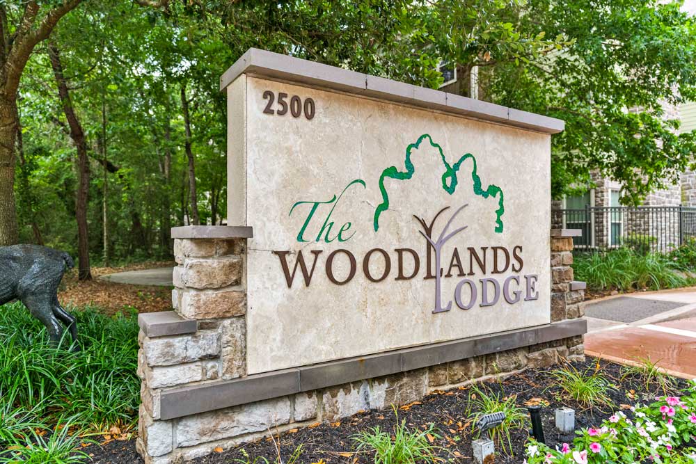 The Woodlands Lodge entrance sign at 2500 with stone columns, deer statue, and surrounding wooded greenery