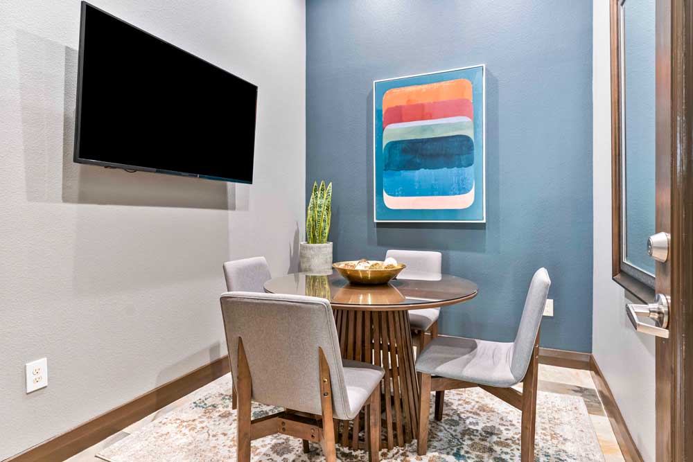 Private meeting space with round table, four chairs, abstract wall art, and wall-mounted TV in apartment community