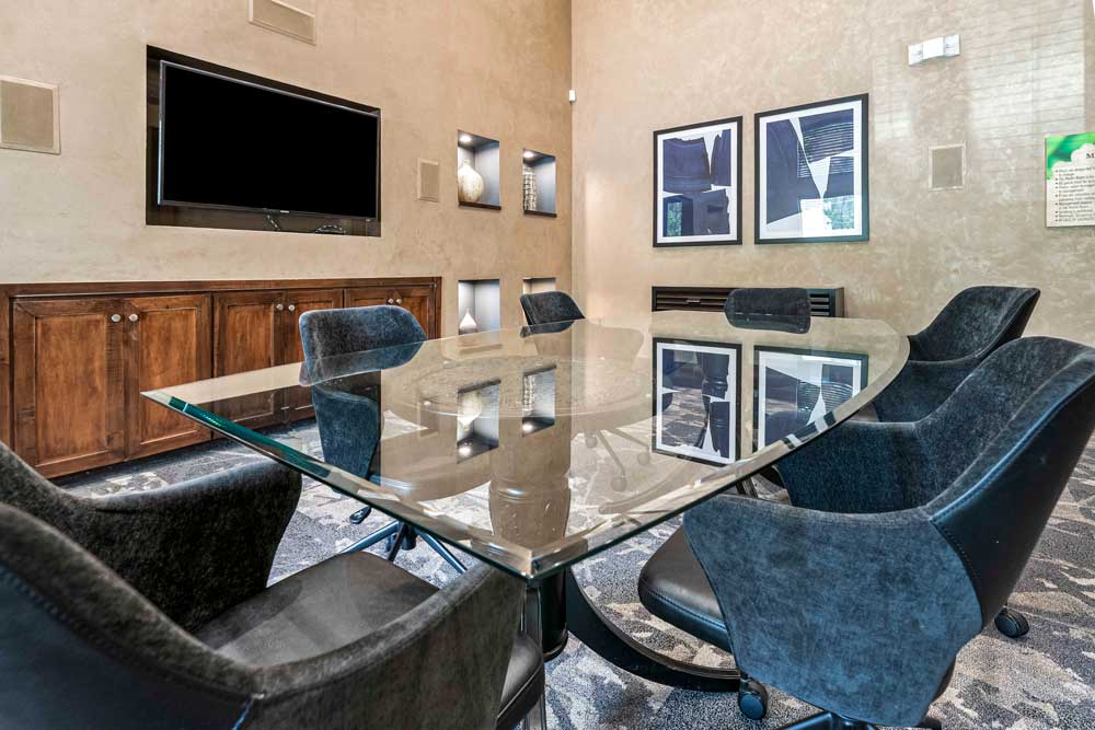 Glass conference table with black chairs, wood cabinet, mounted TV, and accent art inside wall niches