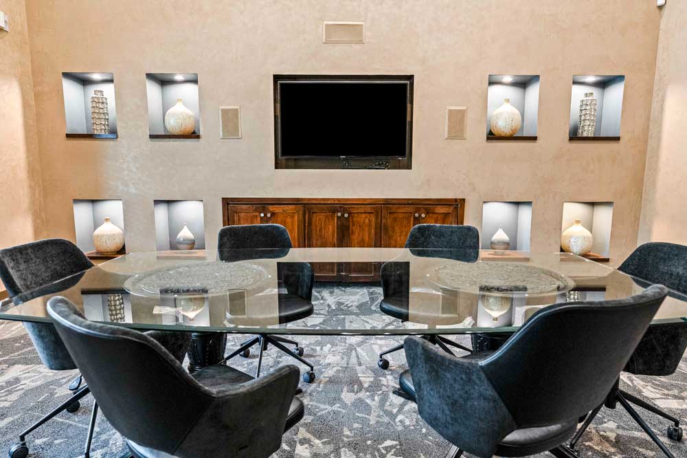 Meeting room with a glass table, dark chairs, built-in wall niches with vases, and a mounted flat-screen TV