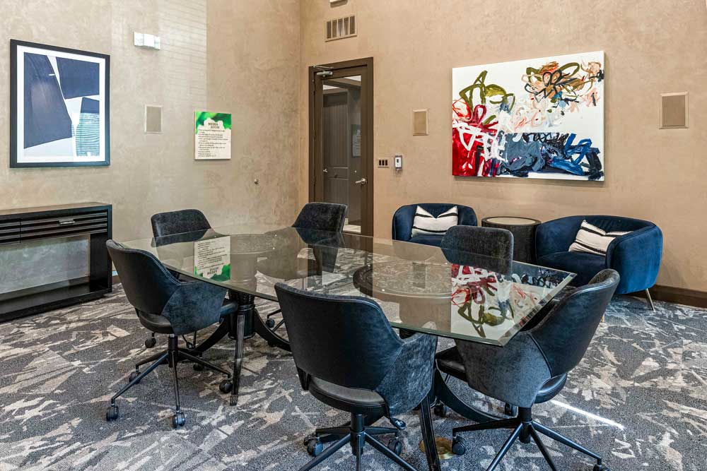 Conference room with a glass table, black chairs, abstract art, and blue lounge chairs with accent pillows