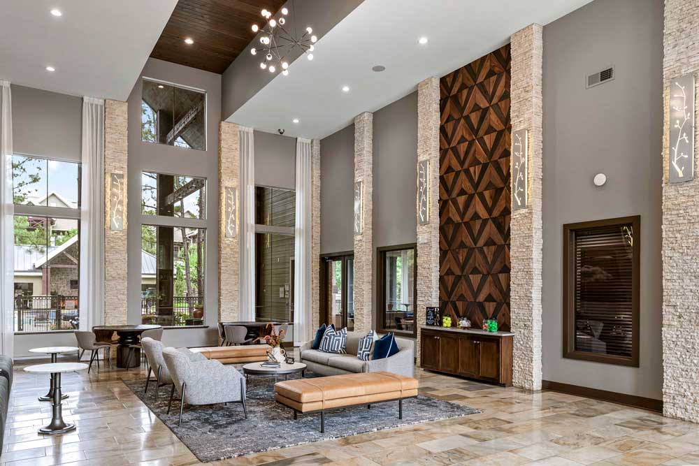 Expansive resident lounge with high ceilings, geometric wood wall, and stylish seating under natural light