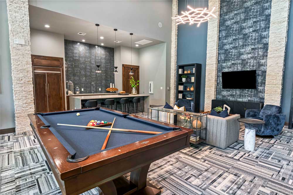 Clubhouse with billiards table, pendant-lit bar, and a sitting area with velvet chairs and accent lighting