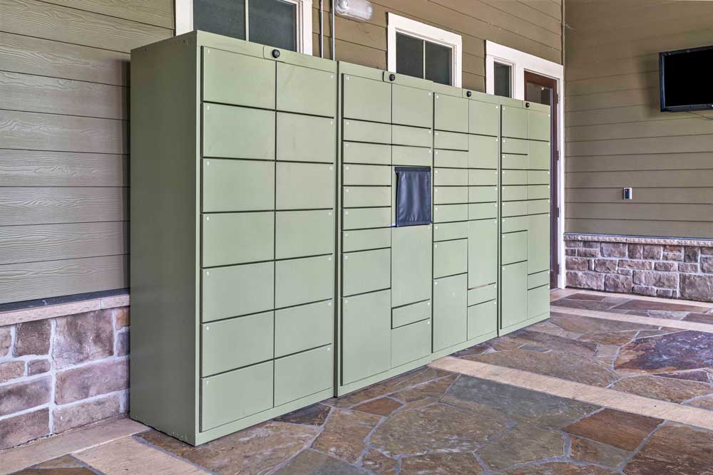 Modern green parcel locker system in a covered outdoor area with stone flooring and wood-paneled walls