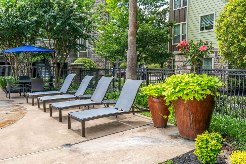 Poolside lounge area with four chairs, tall ceramic planters, a shaded table, and surrounding greenery