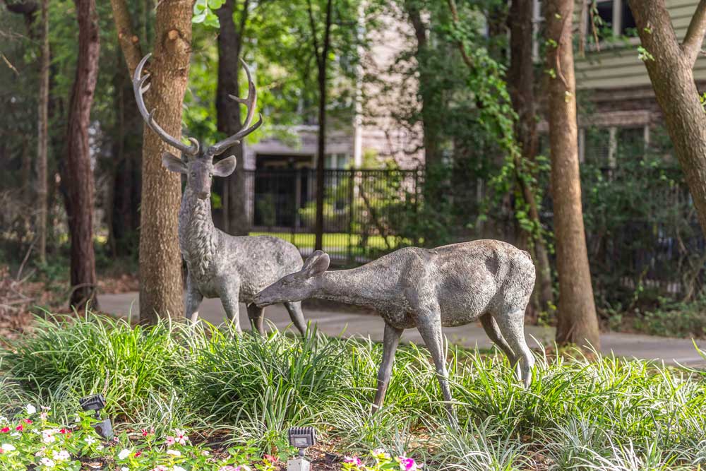 Sculpted deer figures placed in lush greenery near trees and apartment buildings
