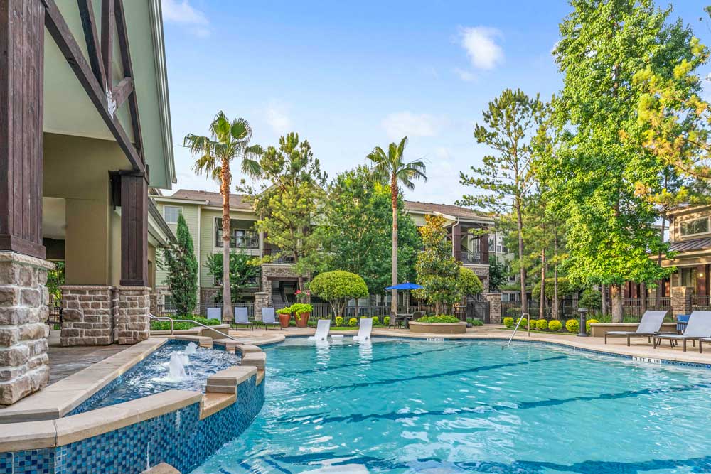 Side view of pool with palm trees, built-in loungers, and apartment buildings under a bright blue sky