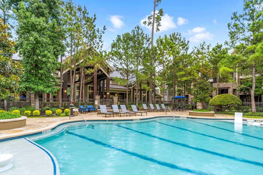 Sparkling pool with lane markers, lounge seating, and manicured gardens under a clear blue sky