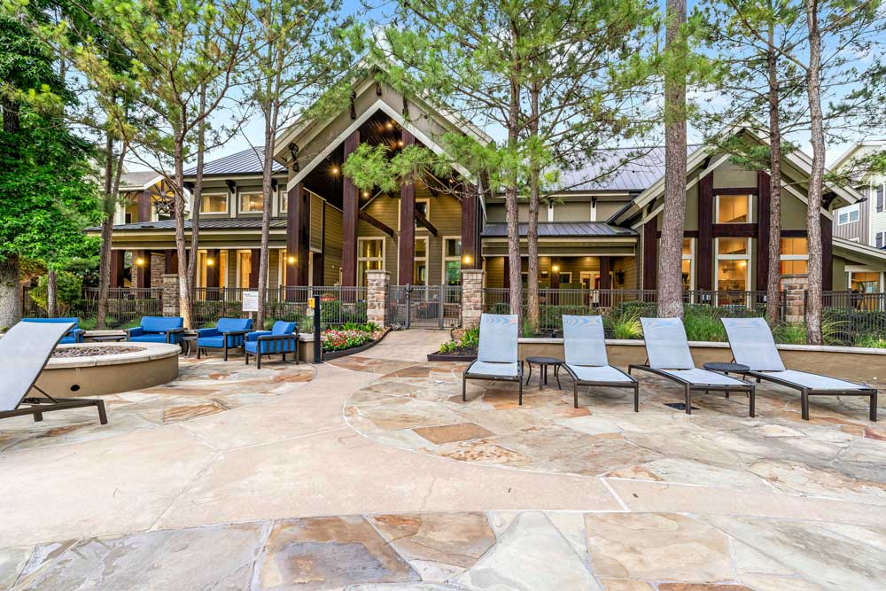 Spacious patio with lounge chairs and a fire pit outside the clubhouse surrounded by trees and soft lighting
