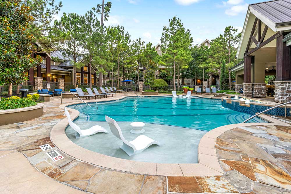 Lagoon-style pool with sun loungers and a clubhouse framed by trees and stone pathways