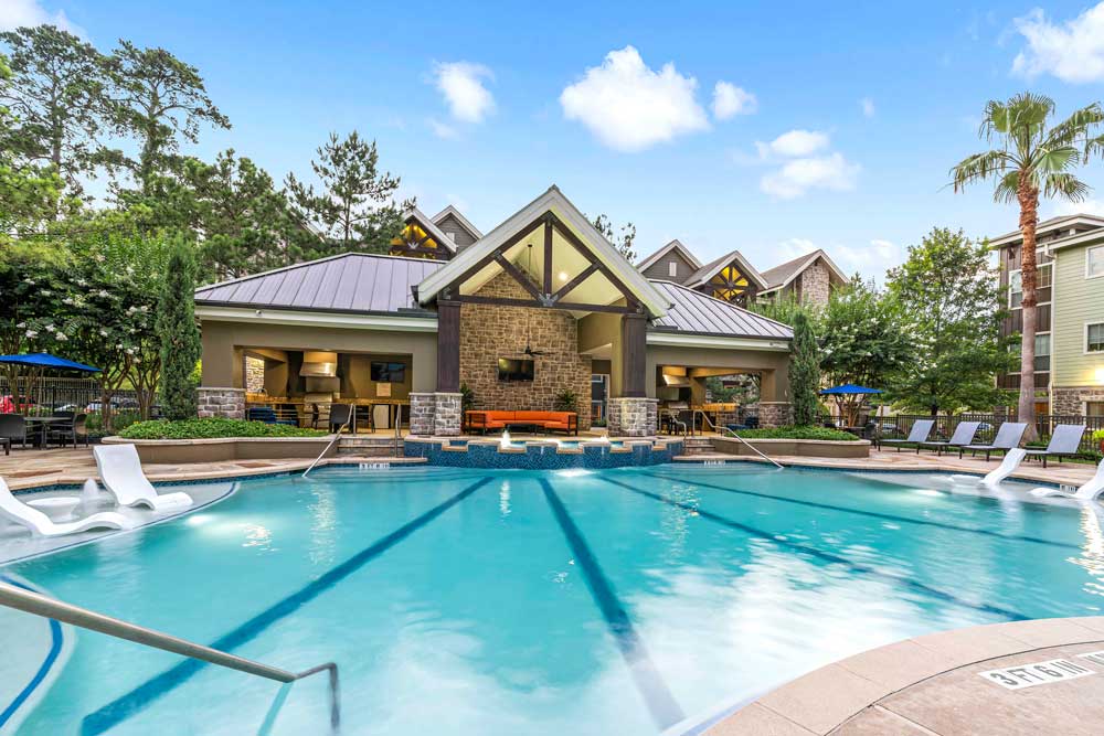 Pool with lap lanes, submerged loungers, and a central clubhouse framed by trees and orange seating